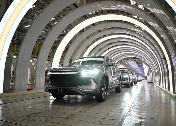 Multiple new energy vehicles from BYD, Tesla, Geely, and Leap Motor are showcased in a modern factory or assembly line with illuminated, curved structural supports, highlighting the rapid growth of global electric and plug-in hybrid car sales in 2025 Q3.