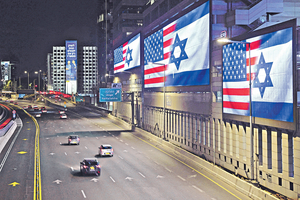 作者认为今次美以联手攻击伊朗,真正幕后黑手是以色列,美方充其量只是帮犯而已。图为以色列特拉维夫高速公路旁的巨型屏幕,正展示美国和以色列的国旗。(路透社资料图片)